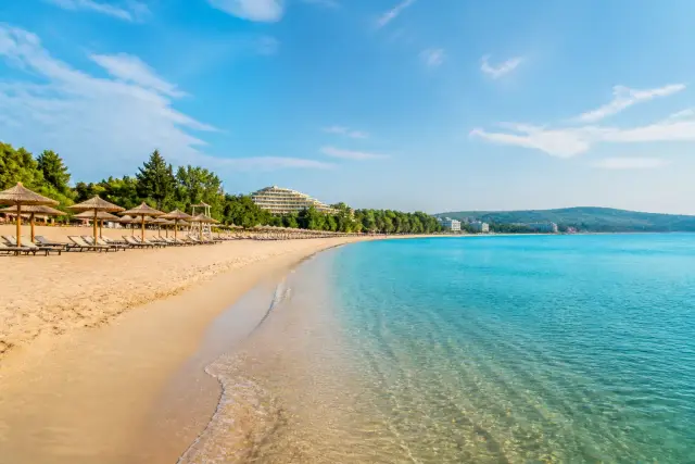 Široká písečná pláž v Albeně u Černého moře s lehátky, slunečníky a hotely v zeleni